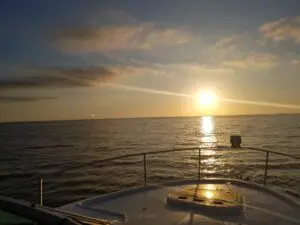 Sunset over calm ocean waters from a boat deck.